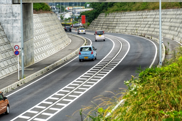 片側二車線の道路を走行する複数の車。手前に水色の軽自動車