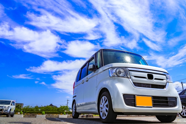 青空の下、駐車場に停められた白い軽自動車