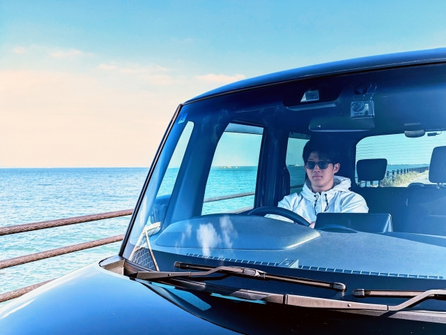 海沿いの道でサングラスをかけ運転する男性
