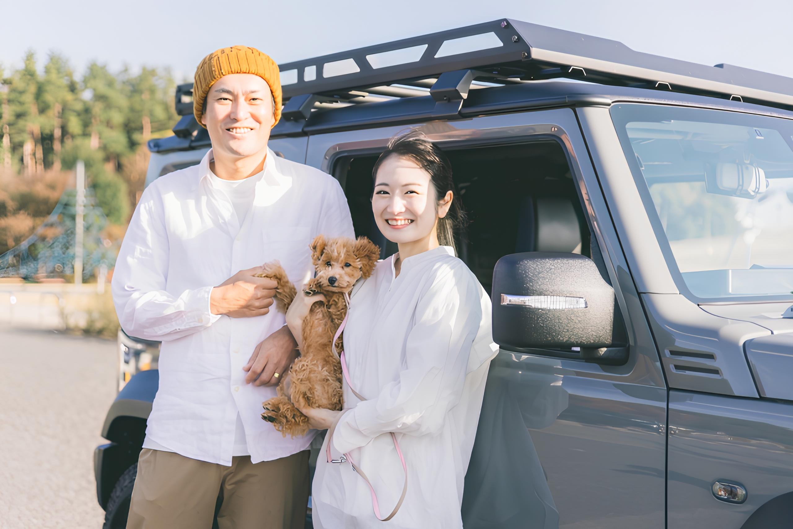 SUVの横で犬を抱いて笑う夫婦